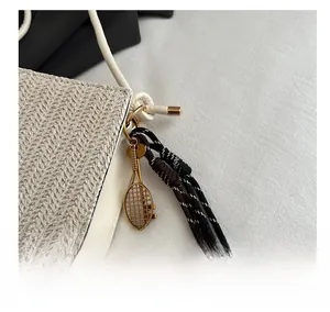 Detail of a beige woven tote bag with a golden tennis racket charm and braided cord