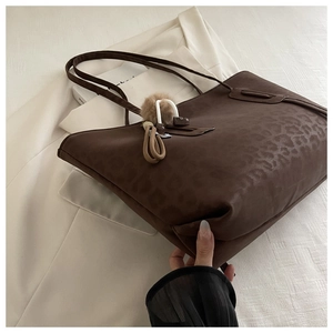 Close-up of leopard print tote bag with brown faux leather texture and plush charm