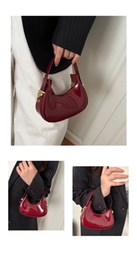Detail of burgundy laser glossy patent leather crescent bag with gold zipper and handle