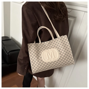 Detail of beige tote bag with M-pattern print and shoulder strap on brown blazer