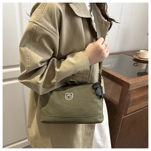 Detail of olive green nylon crossbody bag featuring cute cartoon bear embroidery