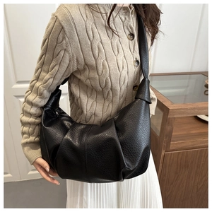 Detail of black pleated croissant bag featuring knotted shoulder strap and pebbled leather texture