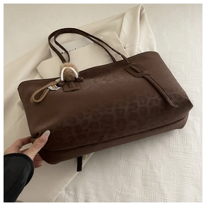 Detail of dark brown leopard print tote bag with fuzzy ball charm on white blazer