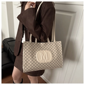 Detail of off-white tote bag with brown M-pattern and embossed logo on model shoulder