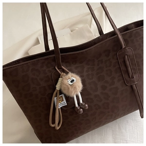Close-up of leopard print tote bag featuring a cute furry doll charm attachment