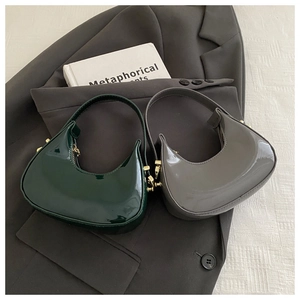 Detail view of two glossy leather crescent bags with gold hardware on a wool blazer