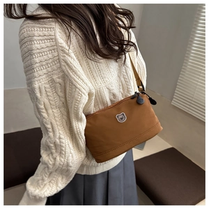 Brown crossbody bag with cartoon bear patch worn by model in a white sweater