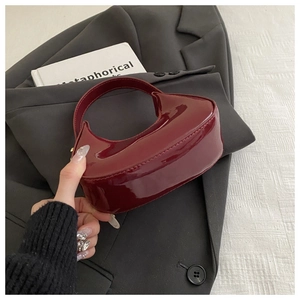 Close-up of a burgundy patent leather mini handbag with glossy finish on grey blazer