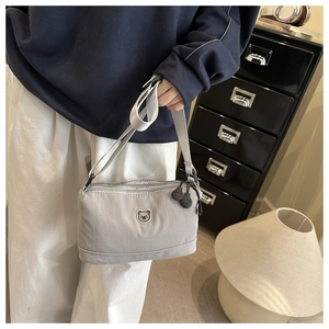 Detail view of light grey crossbody bag with multi-zipper layers and bear embroidery
