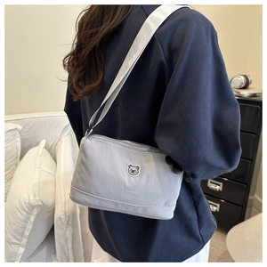 Detailed side view of a light grey nylon crossbody bag featuring a cute bear patch on a model