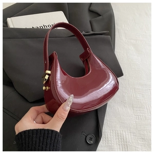 Detail of burgundy patent leather baguette bag showing glossy finish and crescent shape