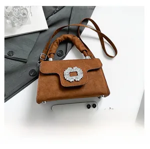 Detail view of brown suede handbag featuring a crystal buckle and ruffled handle grip