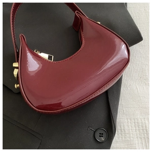 Close-up of wine red patent leather crescent bag with golden hardware on a black blazer