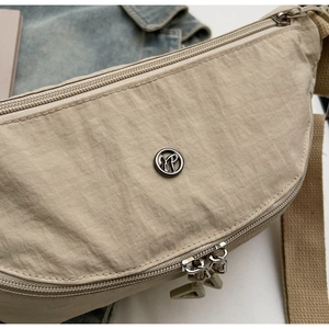 Dettaglio ravvicinato della borsa a tracolla in nylon beige con doppia zip e logo in metallo