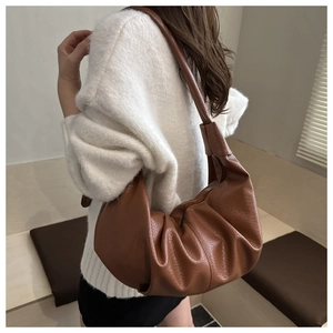 Brown pleated half-moon hobo bag in soft faux leather material shown from a side view