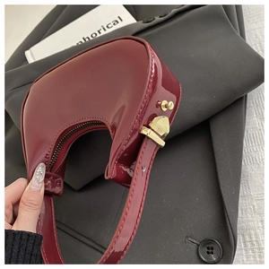 Detail of dark red patent leather hobo bag with gold hardware and crescent shape design