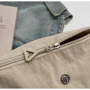 Dettaglio macro della borsa in nylon beige con cerniera argento e fibbia in metallo tonda