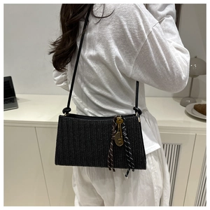 Detail of black woven crossbody bag with gold tennis racket charm and thin shoulder strap