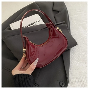 Close-up of wine red patent leather crescent handbag with elegant gold metal hardware
