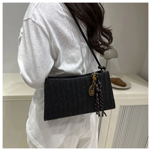 Detail of black woven shoulder bag with golden racquet charm and colorful tassels on model
