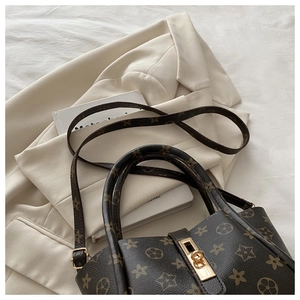 Close-up of a brown monogram tote bag with golden hardware on a white blazer