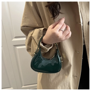 Detail of dark green patent leather crescent bag with top handle and gold hardware