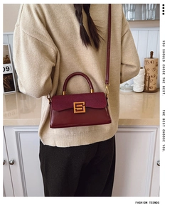 Detail of burgundy leather shoulder bag with gold metal buckle and suede flap texture
