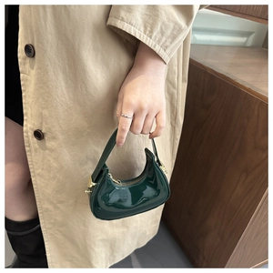 Detail of a dark green patent leather crescent bag with gold zipper and metallic buckle