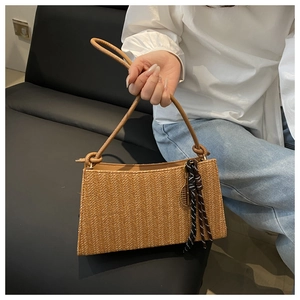 Detail view of a brown woven straw shoulder bag with knot charm and metal pendant