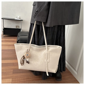 Detail of cream leopard-textured tote bag featuring a cute plush owl charm accessory
