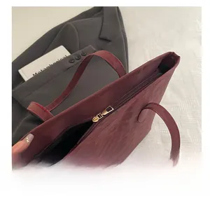 Close-up of smooth gold metal zipper and dark textured leather on burgundy tote bag