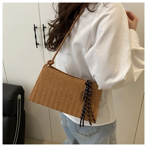 Macro shot of brown straw shoulder bag featuring herringbone weave texture and tassel detail