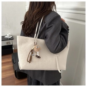 Detail of a large cream tote bag with fine texture and decorative faux fur pompom charm