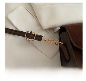 Detail shot of golden metal hooks and suede leather texture on a dark brown shoulder bag