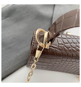 Detail of brown crocodile pattern leather bag showing gold hardware buckle and handle stitching
