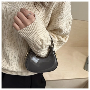 Detail of a dark gray patent leather mini dumpling bag paired with a cozy cable knit sweater