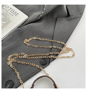 Detail of a golden metal chain strap on brown leather bag with aesthetic props