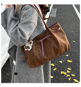Detail of leopard print tote bag with plush charm on gray coat and outdoor setting