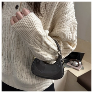 Detail of grey glossy crescent bag with gold hardware worn over a beige knit sweater