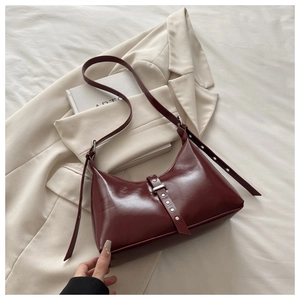 Détail du sac à bandoulière bordeaux avec rivets argentés sur un blazer minimaliste