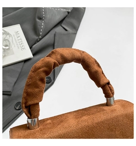 Macro shot of brown suede handbag with ruched handle and silver metal accents
