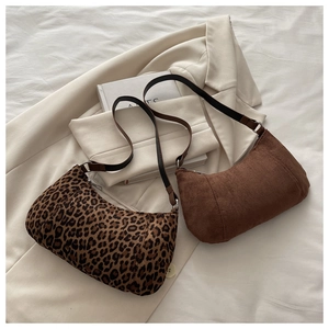 Detail of leopard print and brown suede hobo bags on cream blazer with soft lighting