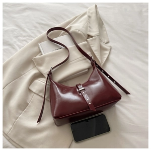 Détail du sac bandoulière bordeaux foncé avec boucle métallique sur literie blanche