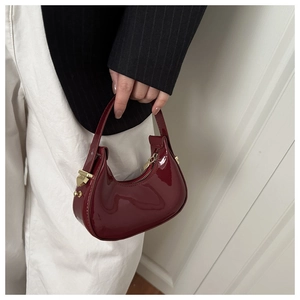 Close-up of glossy wine red crescent bag with shiny gold hardware and patent leather texture