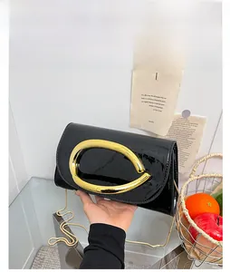 Detail of black patent leather bag with gold ring handle and metallic chain strap