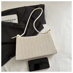 Detail of a minimalist cream woven shoulder bag with knotted strap and gold hardware accents