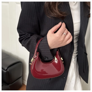 Close-up of a burgundy patent leather crescent bag with gold-tone hardware detail
