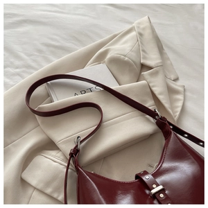 Gros plan d'un sac en cuir verni bordeaux avec boucle argentée et détails de rivets