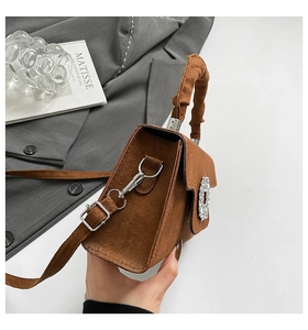 Detail view of brown faux suede handbag featuring arched pleated handle and rhinestone buckle