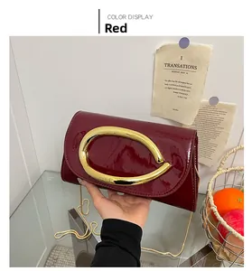 Detail of red patent leather clutch bag with gold horseshoe buckle and chain strap